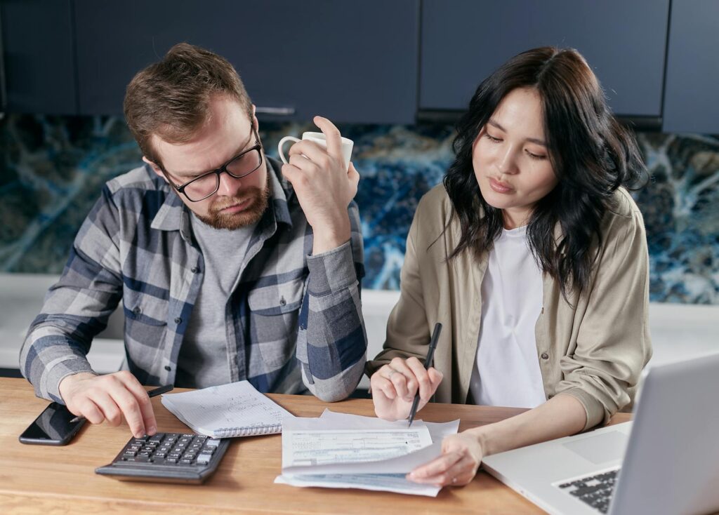 A couple happily using a wedding budget planning calculator on a tablet, surrounded by wedding planning notes and a coffee cup.