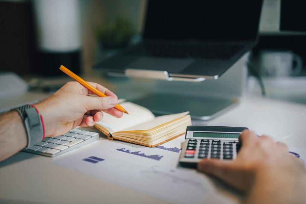 A student using a daily expense tracker on a laptop, with a calculator and coins on the desk, symbolizing effective budget management.