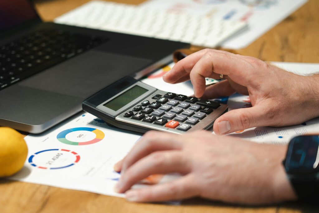 A tourist happily planning their journey using a travel budget calculator on a laptop, with travel icons and a world map in the background, symbolizing a well-organized trip expense planner.